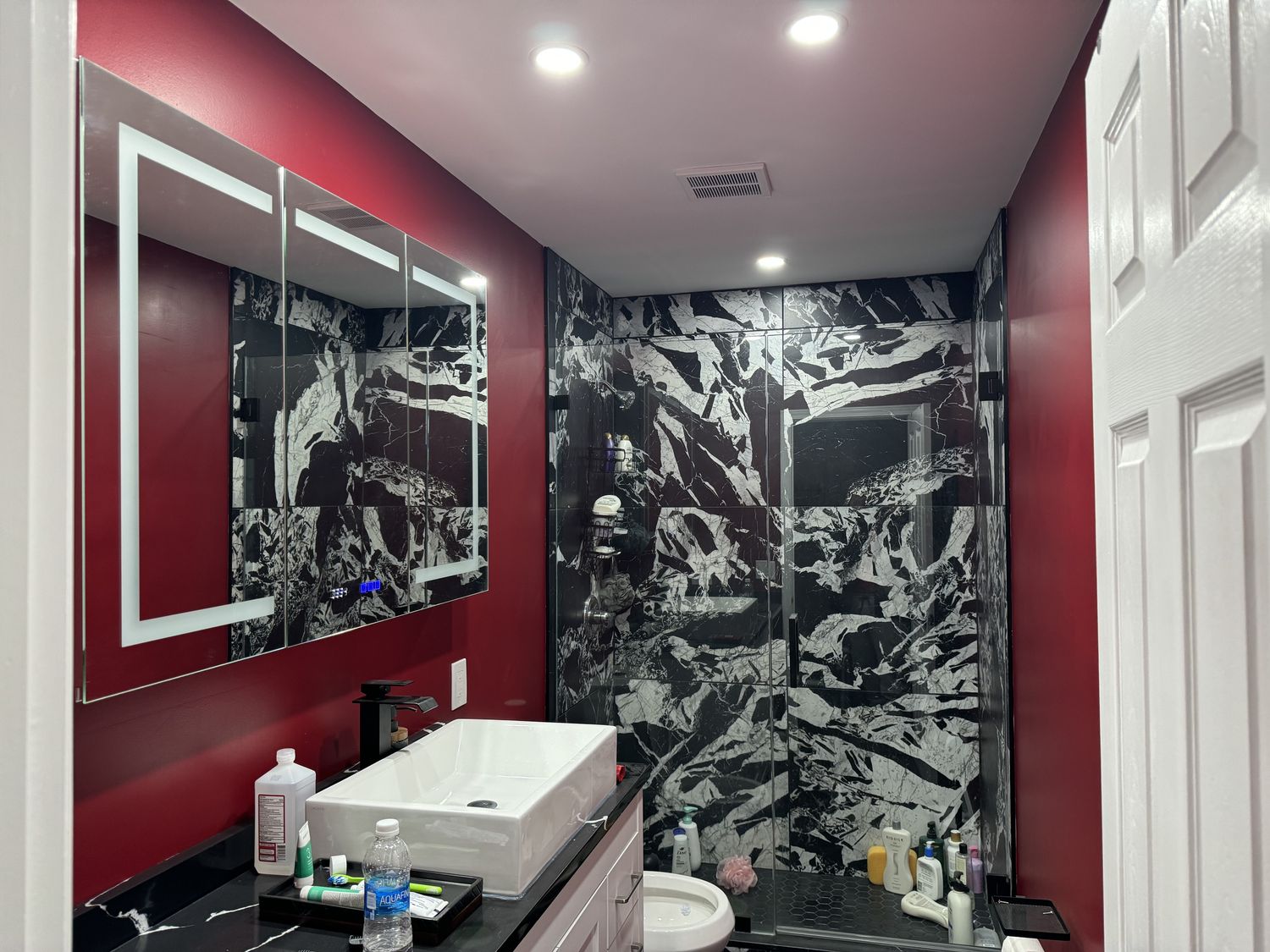 Bathroom with dramatic black marble tile, LED mirror and vessel sink