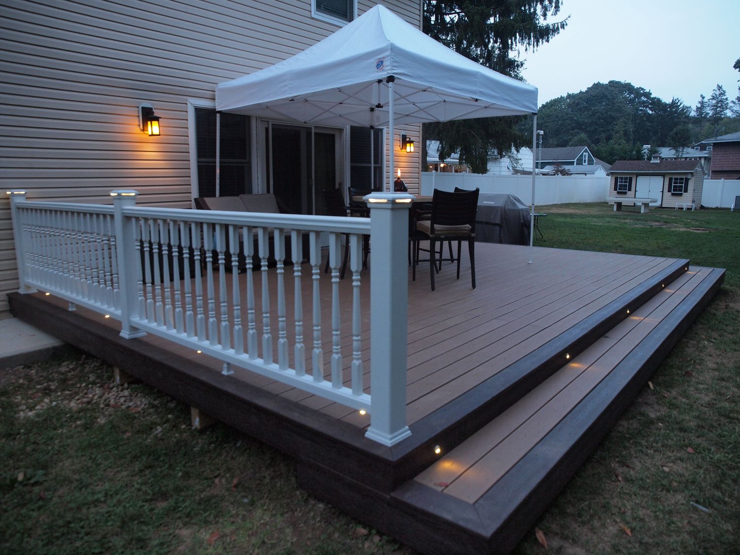 Composite deck with white railings and LED riser lights at dusk