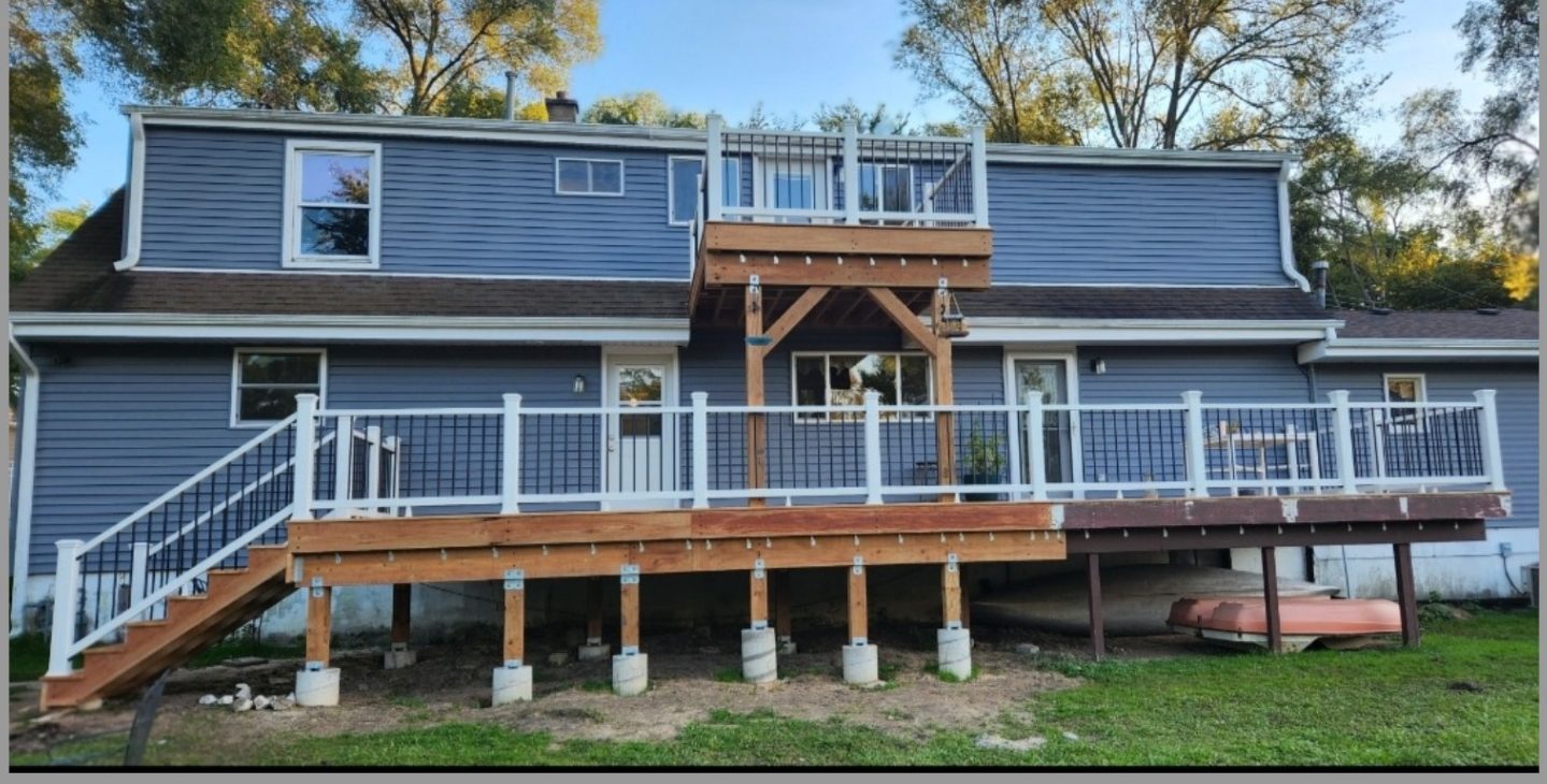 The same lake house with a new multi level deck, white railings and cedar entry