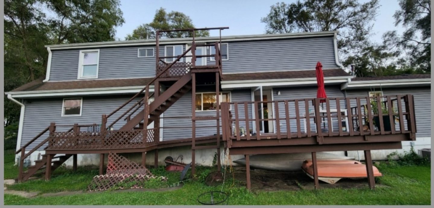 Rear of a lake house with an old weathered brown deck and stairs before rebuilding