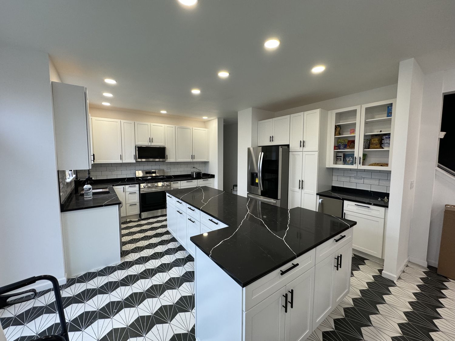 White shaker kitchen with black quartz island and patterned tile floor