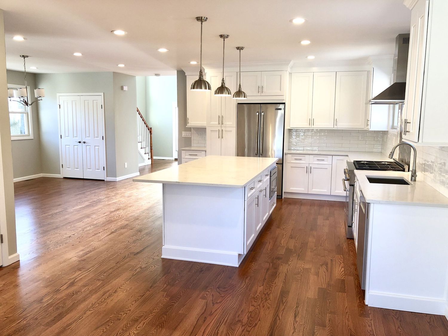 White kitchen with centre island, pendant lights and hardwood floor
