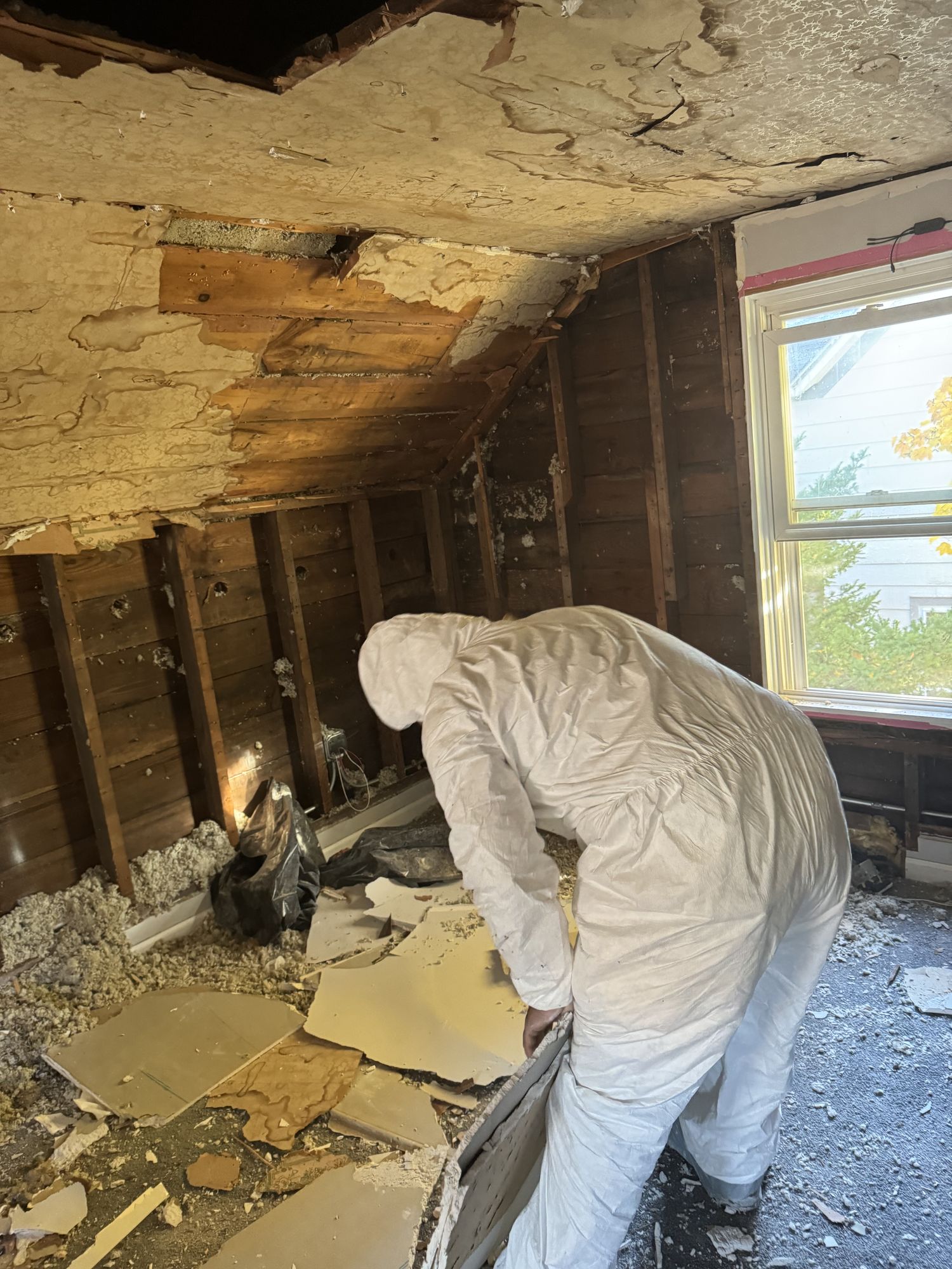 Technician in full protective coveralls removing damaged ceiling material