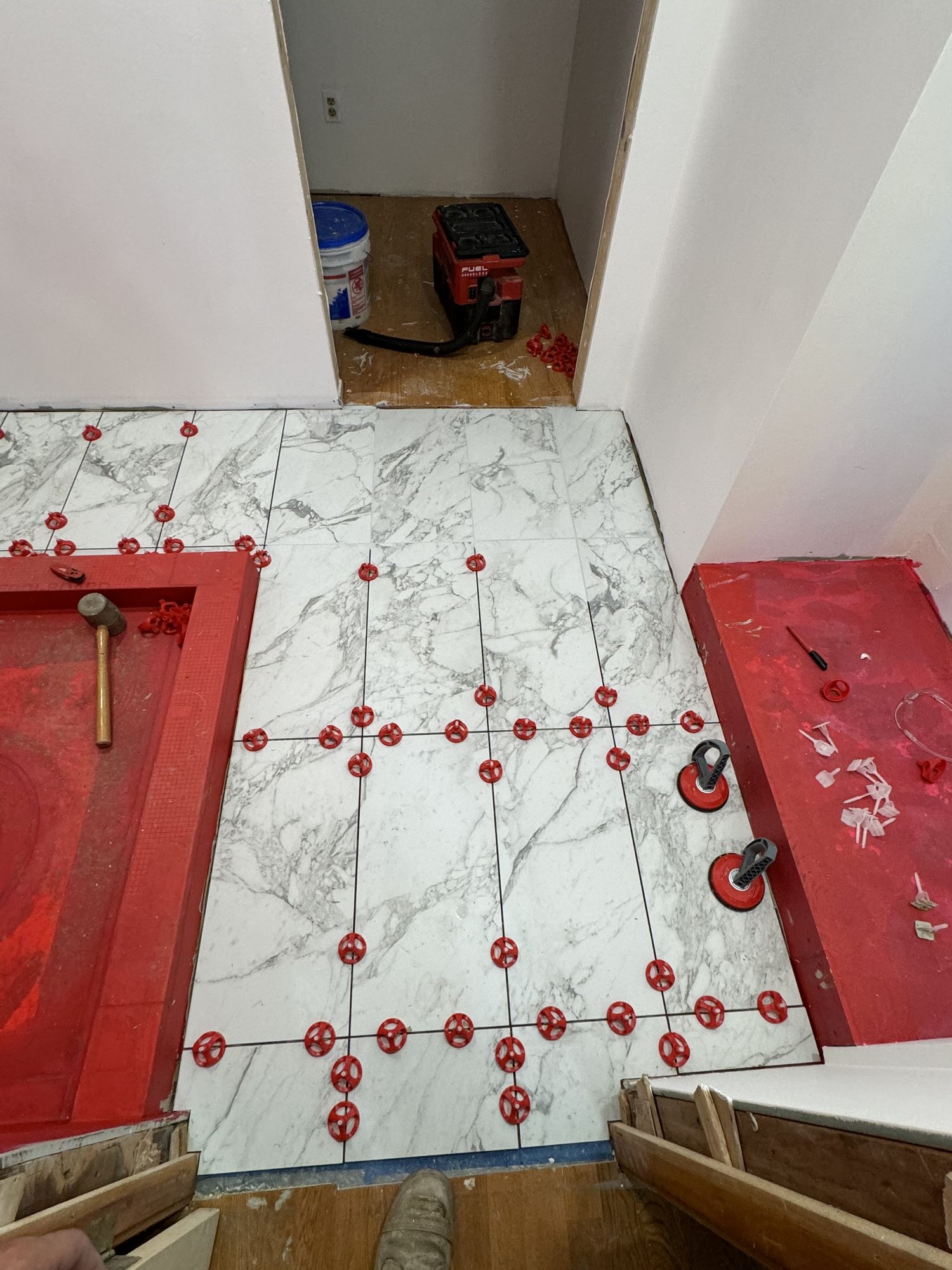 Marble tile set with levelling clips over a red waterproofing membrane